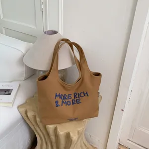 Bolso tote de lona marrón con eslogan bordado en azul sobre un pedestal de diseño
