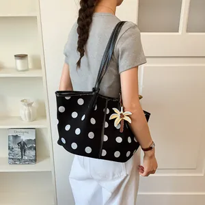 Detailed side view of a stylish black polka dot tote bag with a flower charm shown on a model