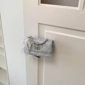 Close-up of a light grey quilted square bag with pearl and lace bow ornament