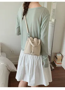 Rear view of a model wearing a beige pebbled leather bucket bag with drawstring detail.
