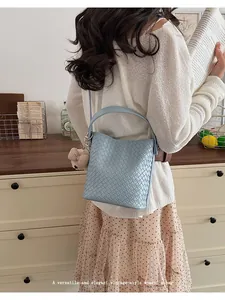 Lifestyle view of a light blue woven bucket bag carried by a model in a vintage setting