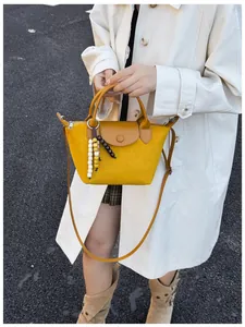 Sac à main jaune en daim pour femme avec breloque en perles sur un trench-coat blanc