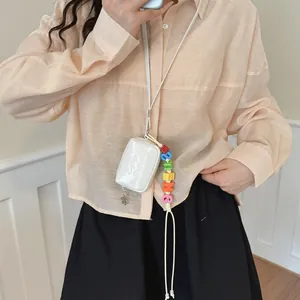 Stylish mini white square crossbody bag featuring a colorful smiling beaded strap detail