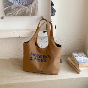 Bolso tote grande de lona marrón con bordado azul 'MORE RICH' y detalle del logotipo