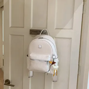 Zaino bianco moderno con trama intrecciata e ciondolo a forma di anatra appeso a una porta.