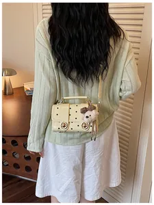 Rear view of a model carrying a vintage cream polka dot crossbody bag with bear pendant