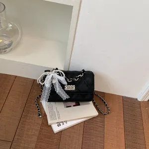 Detail view of a black quilted handbag with pearl strap and white lace bow