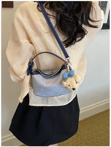 Detailed view of stylish light blue bucket bag with plush bear charm on model's shoulder