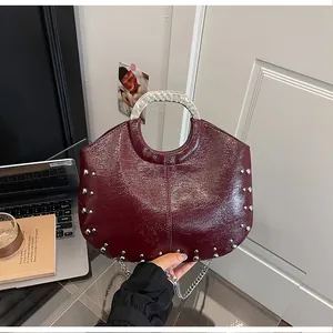 Detailed view of a burgundy glossy handbag featuring silver studs and a metallic handle.