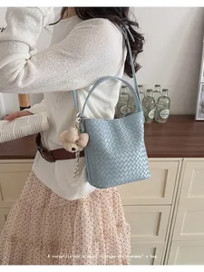 Close-up detail of a light blue woven bucket bag featuring a decorative bear charm