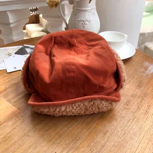 Close-up of burnt orange trapper hat with warm beige plush lining on a wooden table.
