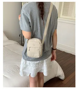 Back view of a woman wearing a cream nylon crossbody phone bag in a bedroom setting.