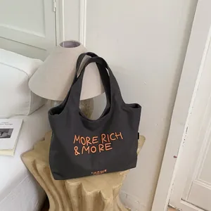 Bolso tote grande de lona gris oscuro con bordado naranja MORE RICH & MORE en habitación