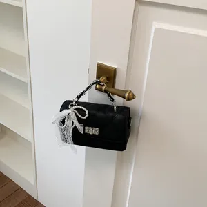 Black quilted square bag hanging on a door handle with lace and pearl charm detail