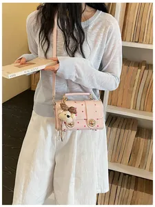 Stylish pink polka dot crossbody bag with a plush bear charm detail on a model.