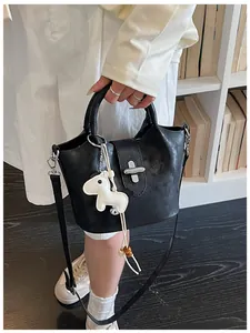Détail d'un sac seau noir design avec breloque cheval tenu à la main.