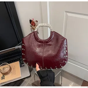 Close-up of burgundy studded handbag featuring a metallic top handle and elegant chain strap.