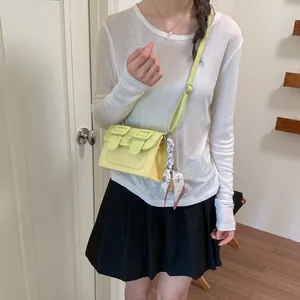 Elegant yellow crossbody square bag with decorative scarf accessory shown on model