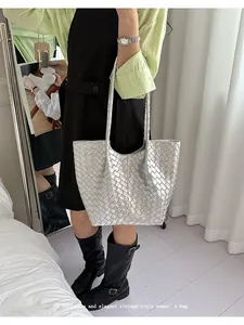 Detailed view of a stylish silver woven tote bag held by a model in a chic indoor setting.