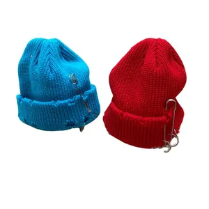 Distressed knitted beanies in blue and red featuring oversized safety pin decorations