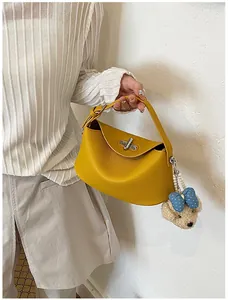 Detail view of a yellow leather handbag with a cute teddy bear charm and turn-lock.