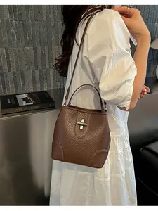 Sac seau en cuir grainé marron avec fermoir en T élégant présenté dans un cadre lifestyle
