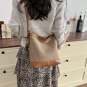 Detail view of the woven straw bucket bag with brown leather trim worn by a model