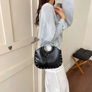 Black studded handbag with metallic chain strap worn by model in a stylish indoor setting.