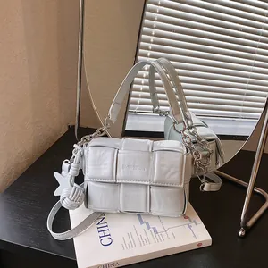 Close-up detail of a minimalist light blue woven leather shoulder bag displayed on a book