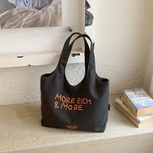 Vista detallada de un bolso tote de lona negra con bordado naranja More Rich & More