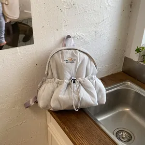 Detalle del bolsillo delantero con cordón y del logotipo bordado en la mochila gris