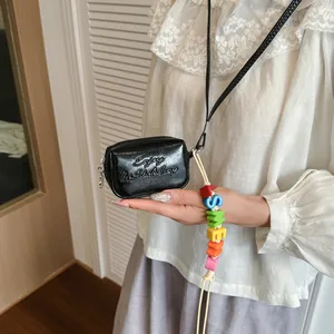 Close-up detail of black glossy mini crossbody bag with embossed text and colorful charm