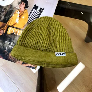 Detailed view of children's olive green knitted beanie with PPSW label on magazine prop.