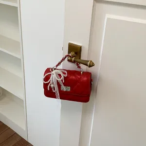 Close-up of a stylish red quilted handbag with pearl bow hanging on a door handle