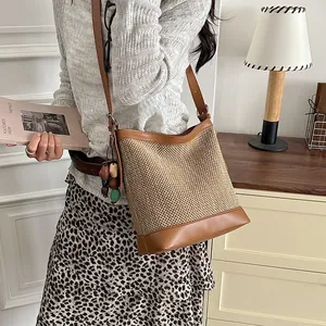 Elegant straw woven bucket bag with brown leather trim and colorful bead charm on model