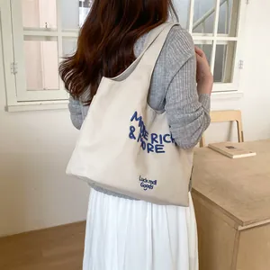 Bolso tote de lona beige informal con bordado azul llevado al hombro por una mujer
