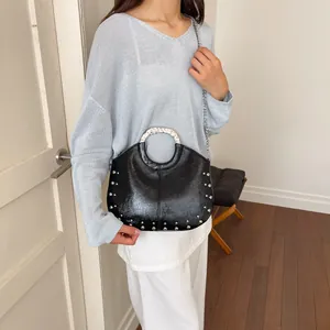 Elegant black glossy handbag with silver studs and metal ring handle shown on model.