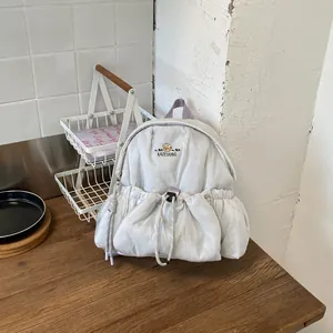 Mochila pequeña acolchada con detalle de oso sobre una mesa de madera.