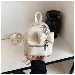 Detail eines cremeweißen Mini-Rucksacks mit dekorativem, großem Schleifenanhänger