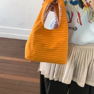 Detailansicht einer orange gestreiften Stoff-Beuteltasche, von einem Model gehalten.