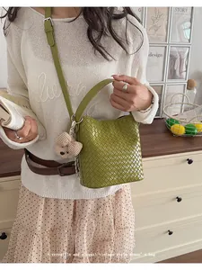 Lifestyle view of an elegant green woven bucket bag featuring a cute teddy bear charm.