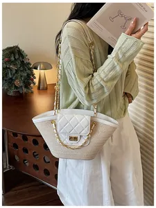 Détail d'un sac cabas en paille tressée avec rabat matelassé blanc et chaînes dorées