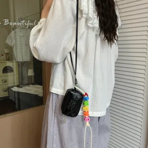 Side view of a mini black crossbody bag with colorful letter charms on a model