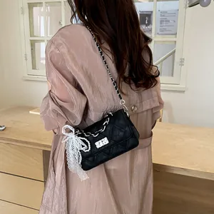 Detail view of a black quilted crossbody bag featuring a white lace and pearl bow charm.
