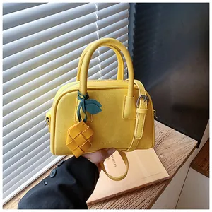 Detailed shot of yellow textured leather bowling bag with charm and shoulder strap.