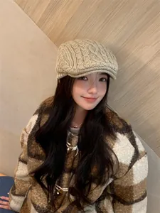 Model wearing a beige knitted newsboy cap with retro cable pattern in a cozy setting