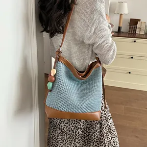 Woven blue and brown bucket bag shown worn on a model's shoulder in a warm room