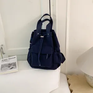 Detalle de la mochila de lona azul marino con cordón sobre un sofá blanco con un libro.