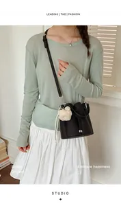 Fashionable black bucket shoulder bag with plush charm worn by a stylish model