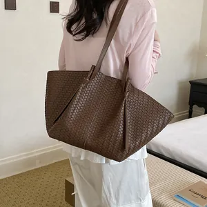 Large brown woven leather tote bag for women presented in a minimalist lifestyle setting